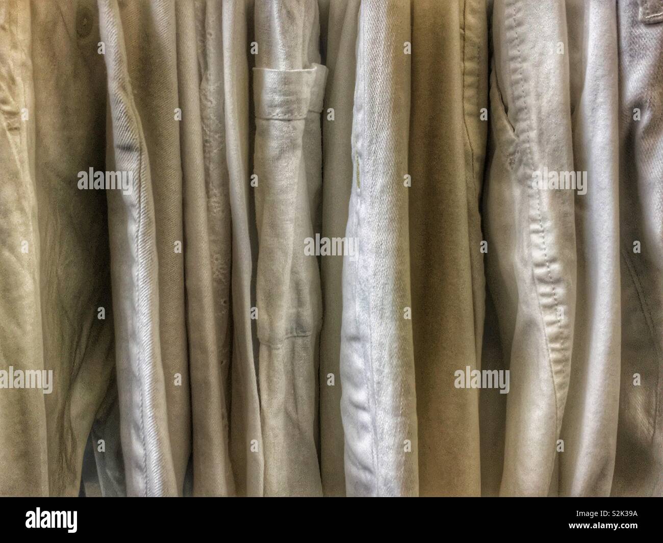 Side view of many fashionable gold hued clothes hanging on a clothing rack. - Smartphone Captured Stock Image