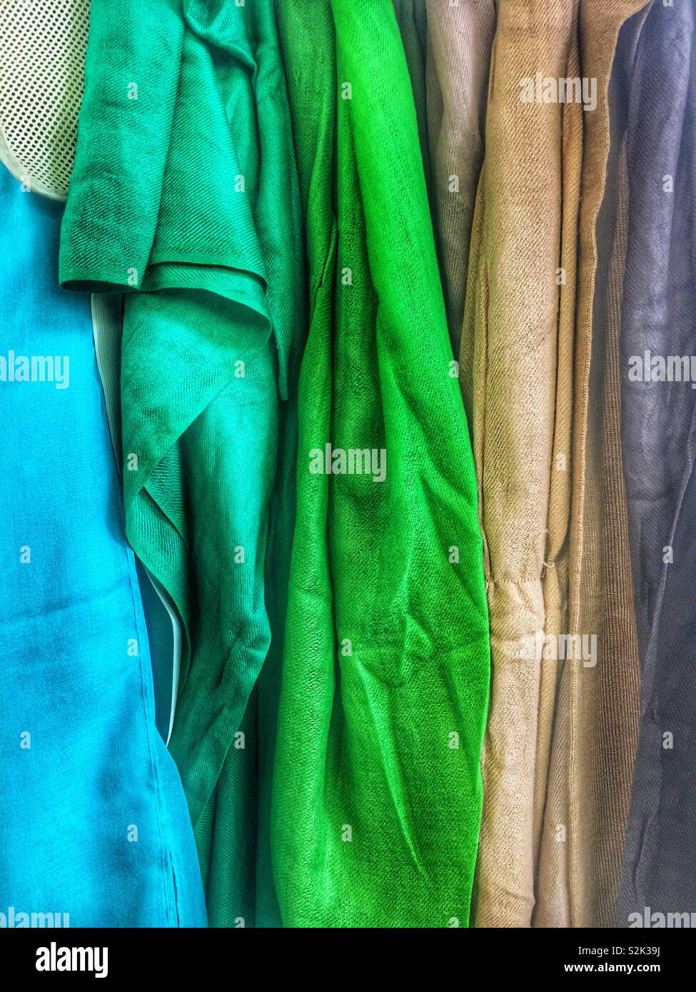 Side view of many fashionable spring color hued scarves hanging on a clothing rack. - Smartphone Captured Stock Image