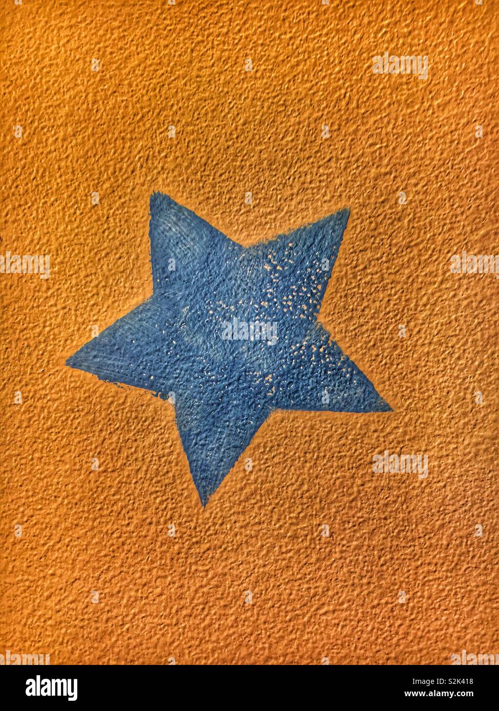 Five pointed blue star painted on an orange background wall. - Smartphone Captured Stock Image
