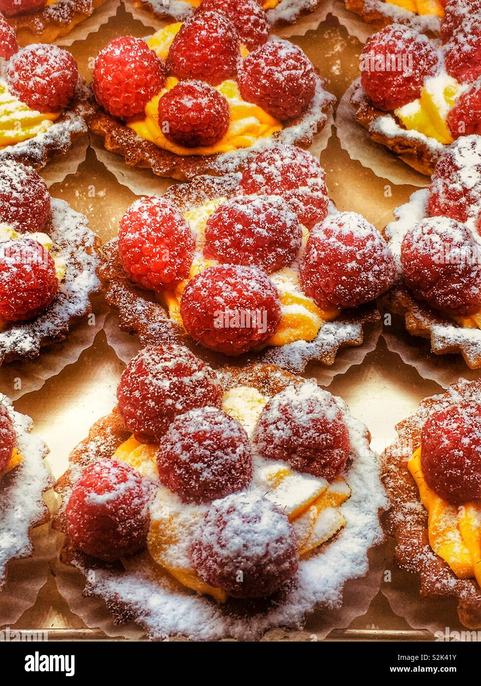 Fresh delicious and mouth watering professionally baked raspberry tarts with cream and powdered sugar. Stock Photo