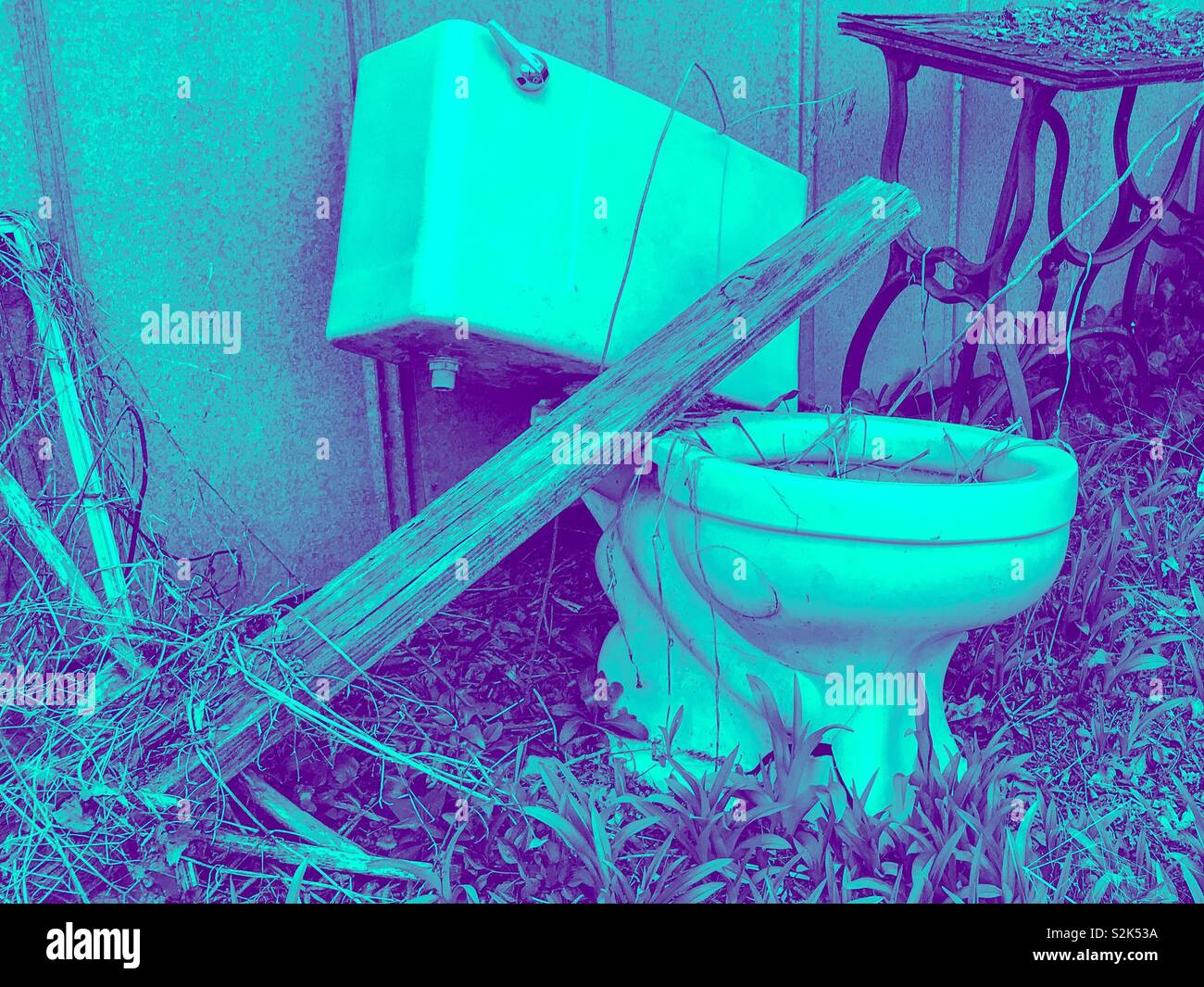 Aqua and purple duotone photo of castoff toilet and vintage sewing machine base beside old metal shed wall - Smartphone Captured Stock Image