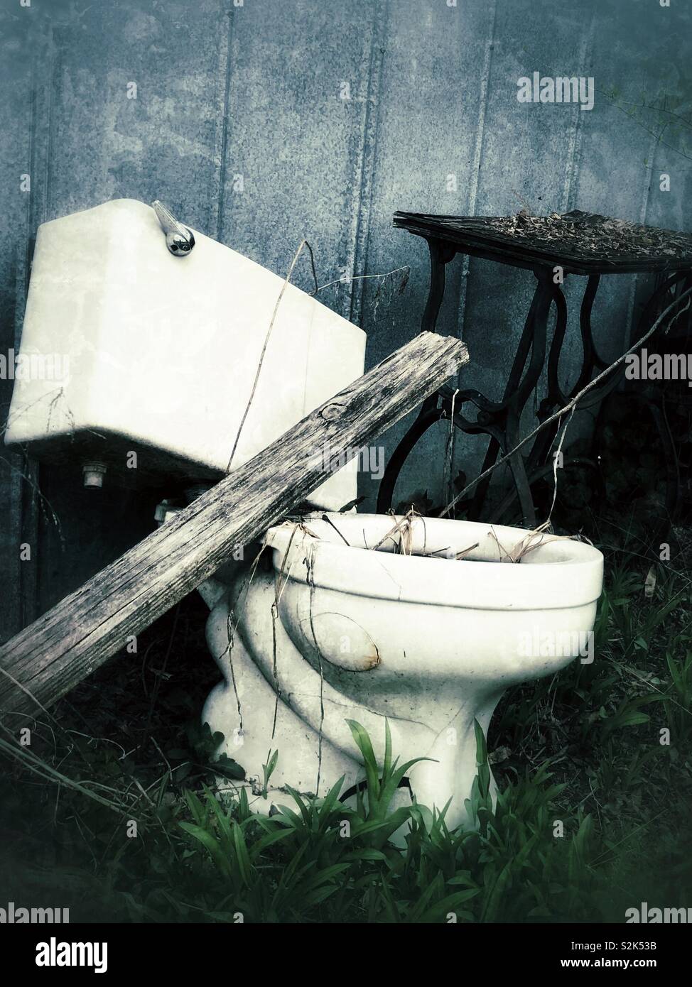 Grunge photo of old castoff toilet and vintage sewing machine base beside metal shed wall - Smartphone Captured Stock Image