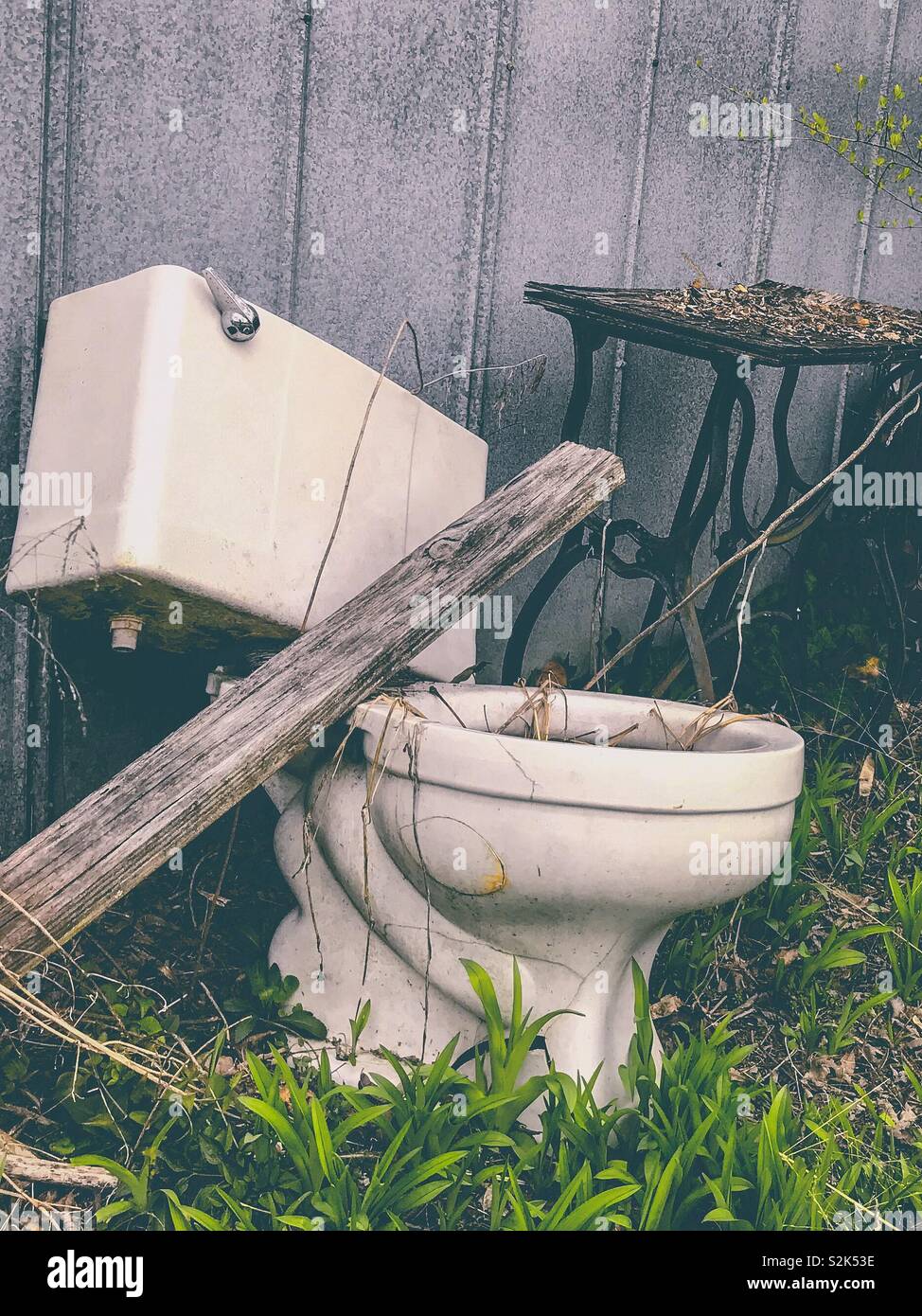 Matt photo of old toilet and vintage sewing machine base beside metal shed wall Stock Photo