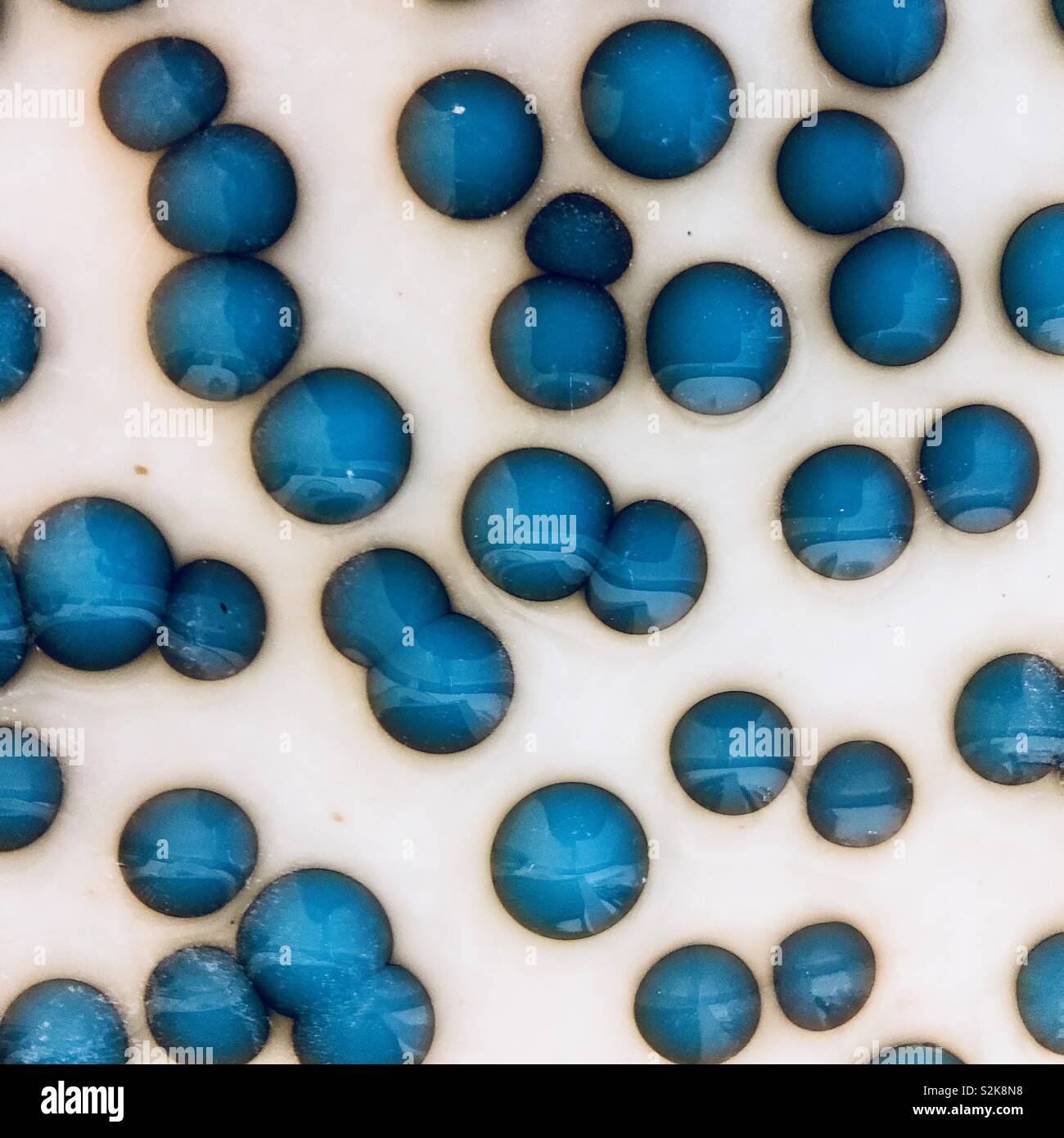 Turquoise blue glass dots on pale vanilla glass made by hand shows chemical reactions between two different glasses Stock Photo
