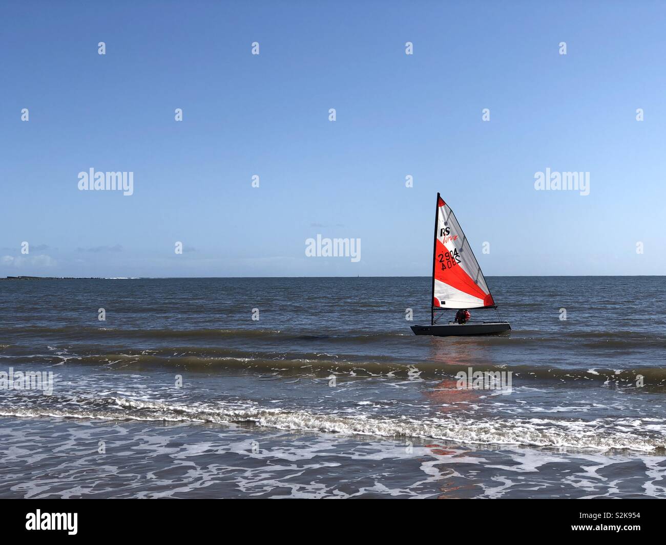 Sailing boat with red and white sail coming back to shore - Smartphone Captured Stock Image