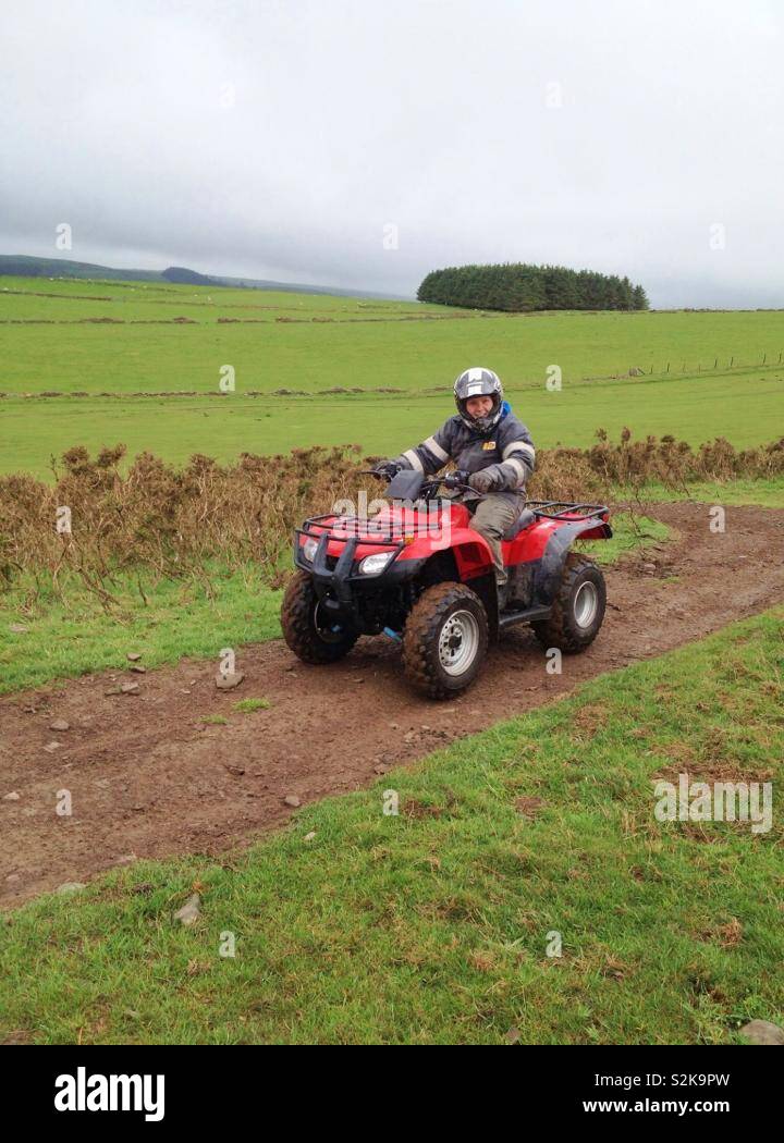 Person riding red quad bike across fields Stock Photo - Alamy