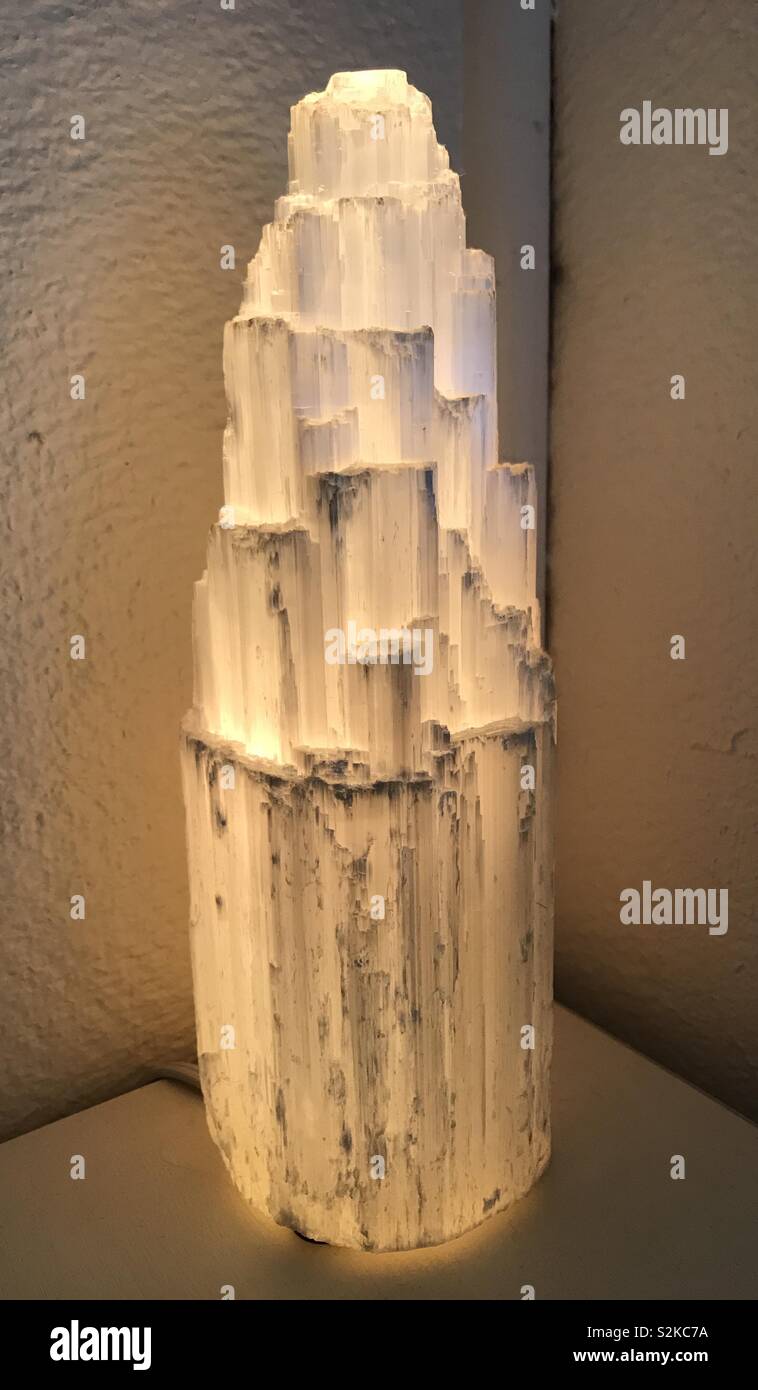 Selenite crystal tower lamp glowing on end table Stock Photo