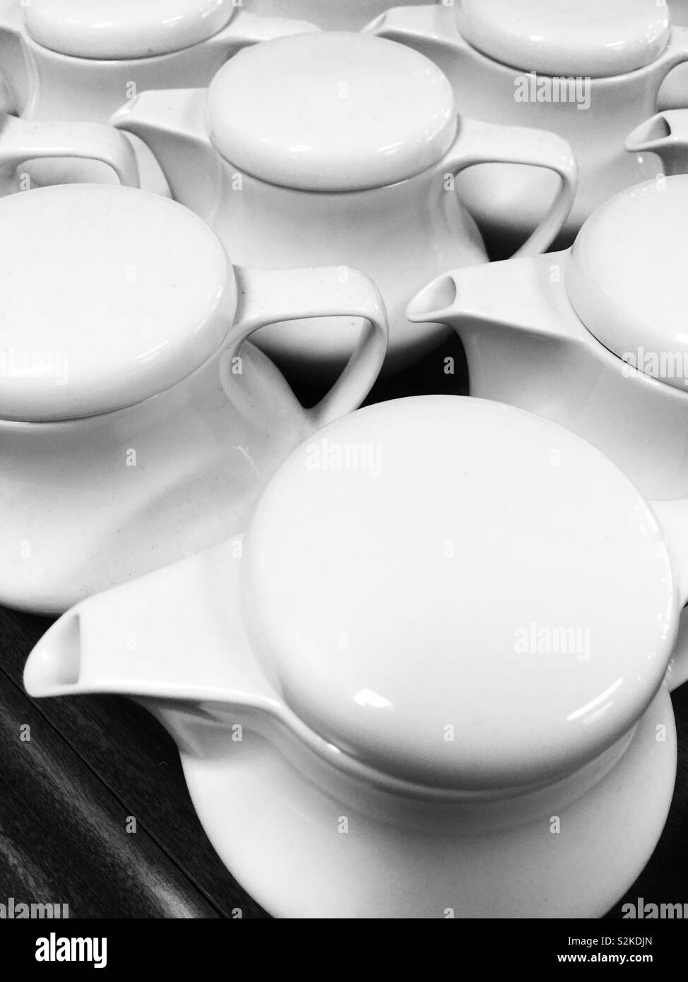 Closeup of group of white teapots on black table. Still life cafe, restaurant background of white ceramic teapots. Stock Photo