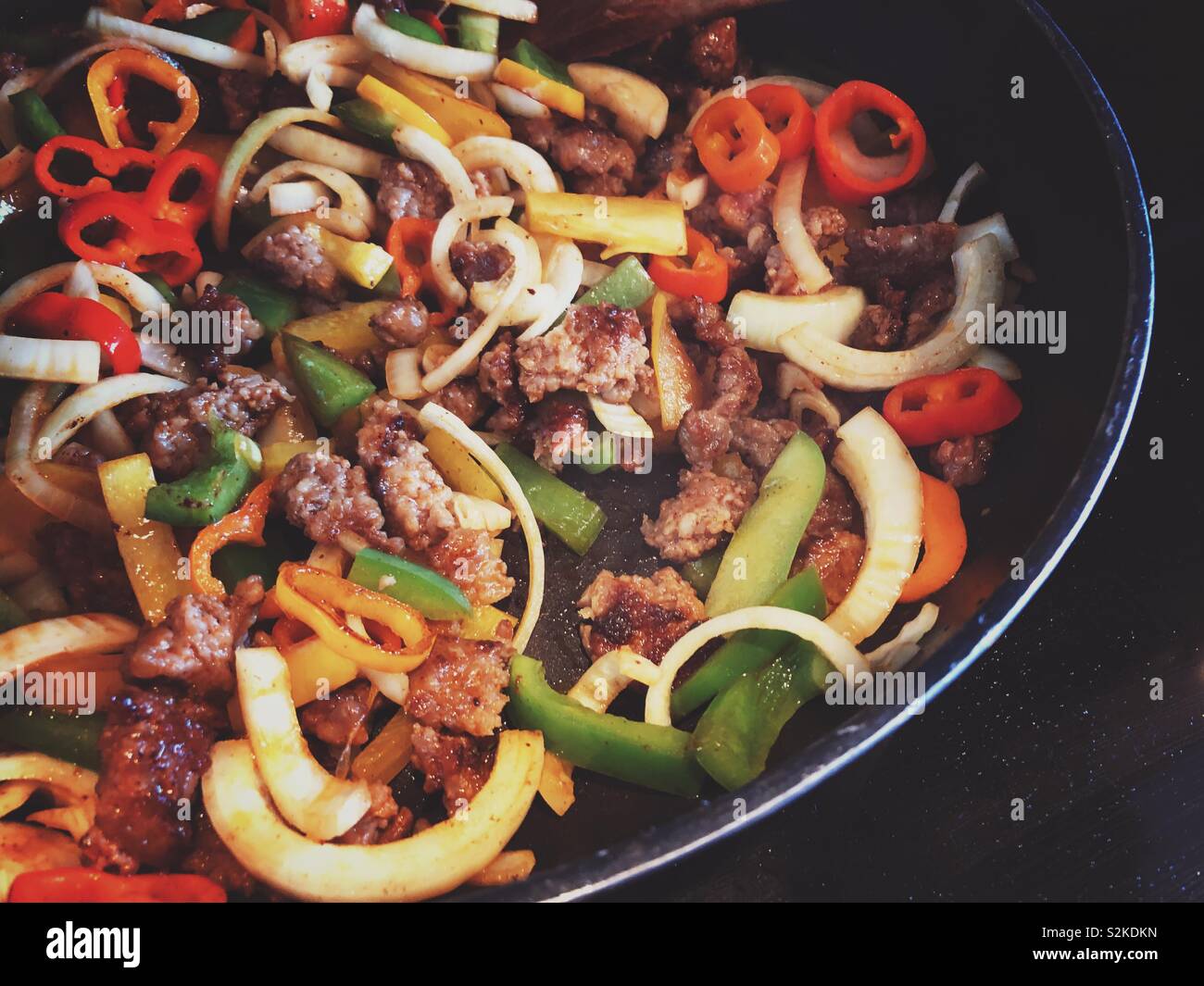 Closeup of hot Italian sausage being sautéed in a black frying pan with onions and colourful peppers - Smartphone Captured Stock Image