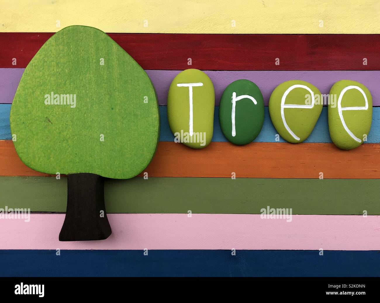 Tree concept with a wooden tree miniature and green stones text over a multi colored wooden board - Smartphone Captured Stock Image