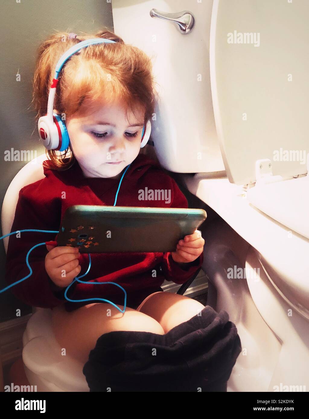 Toddler girl string on potty with tablet and headphones in a bathroom - Smartphone Captured Stock Image