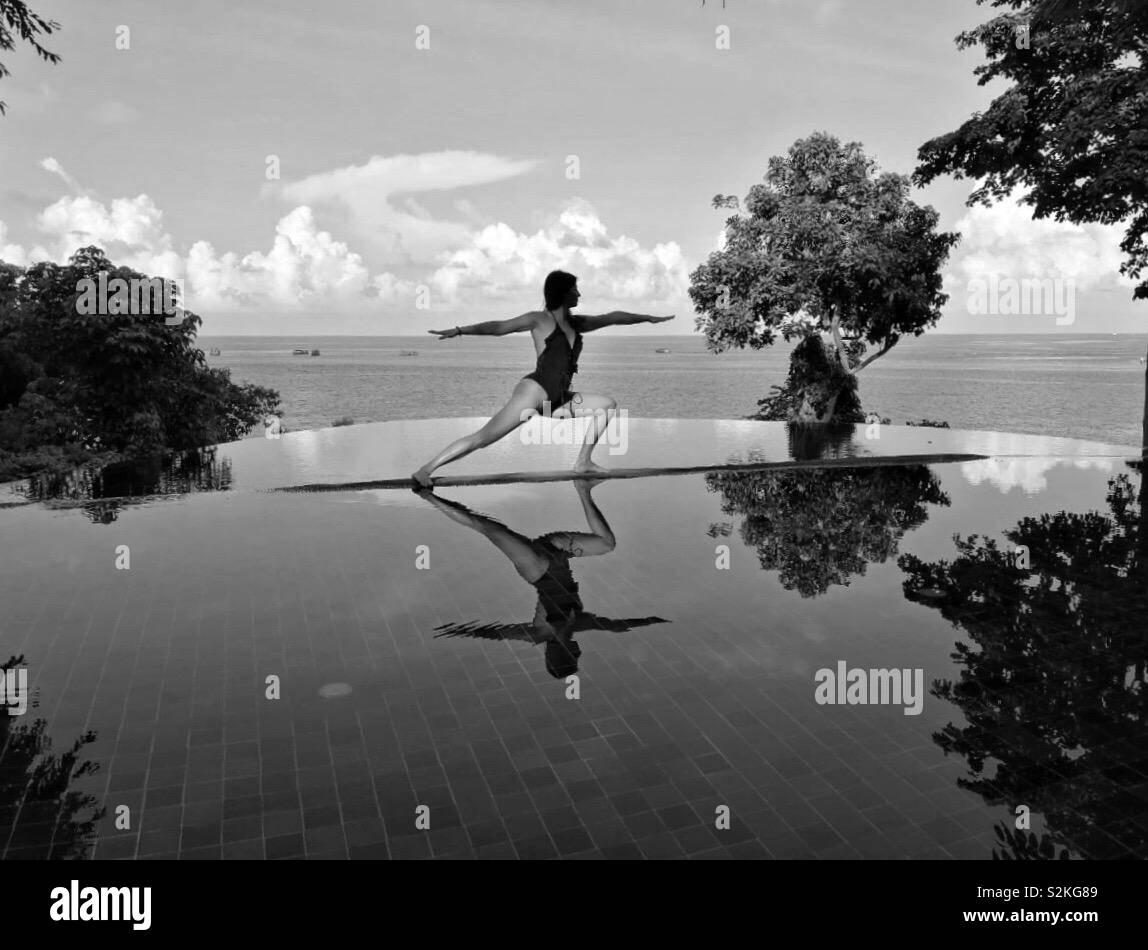 Black and white shot of the young woman making yoga warrior pose by the swimming pool in Thailand Stock Photo