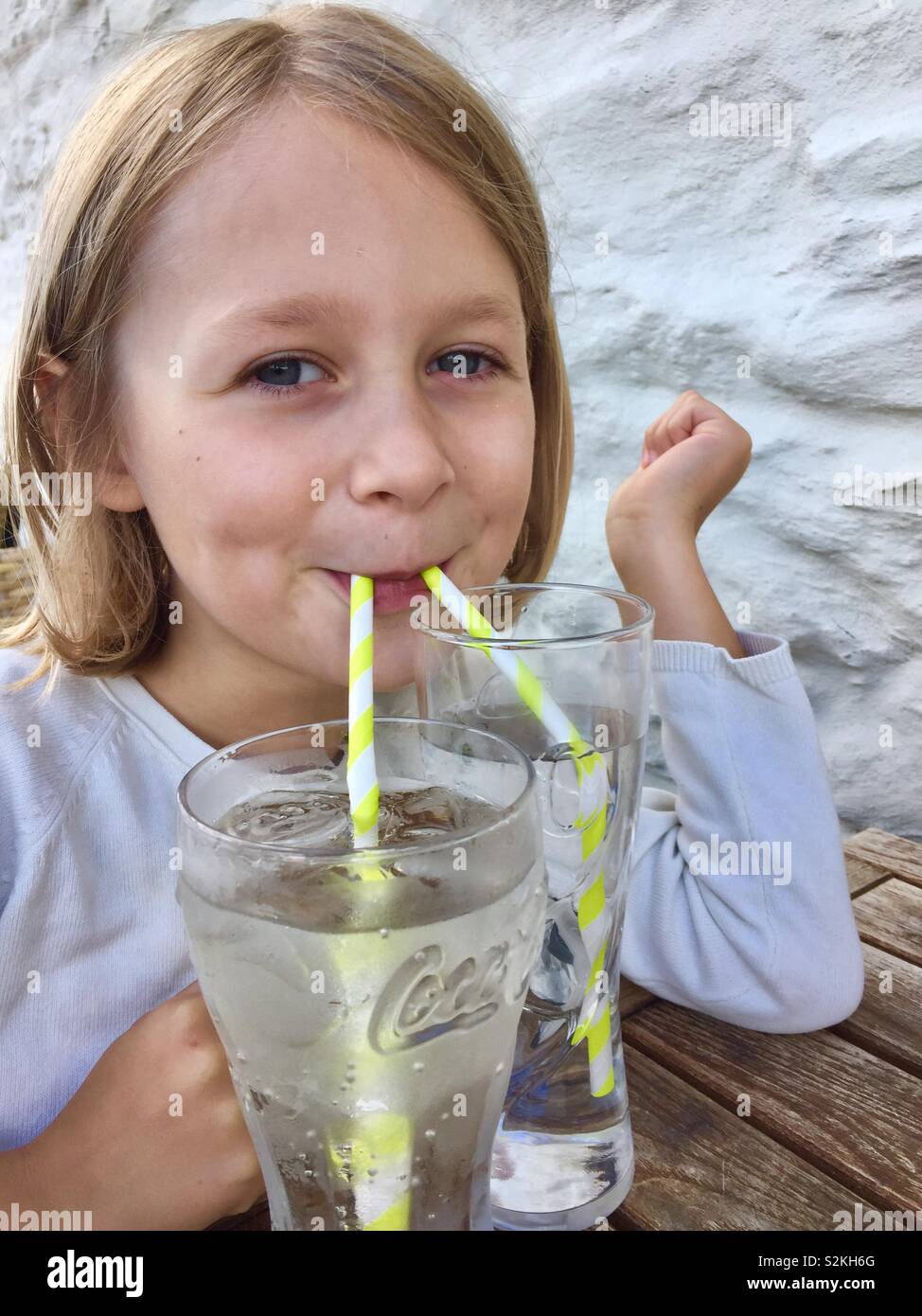 Female child drinking out of two glasses with two straws Stock Photo