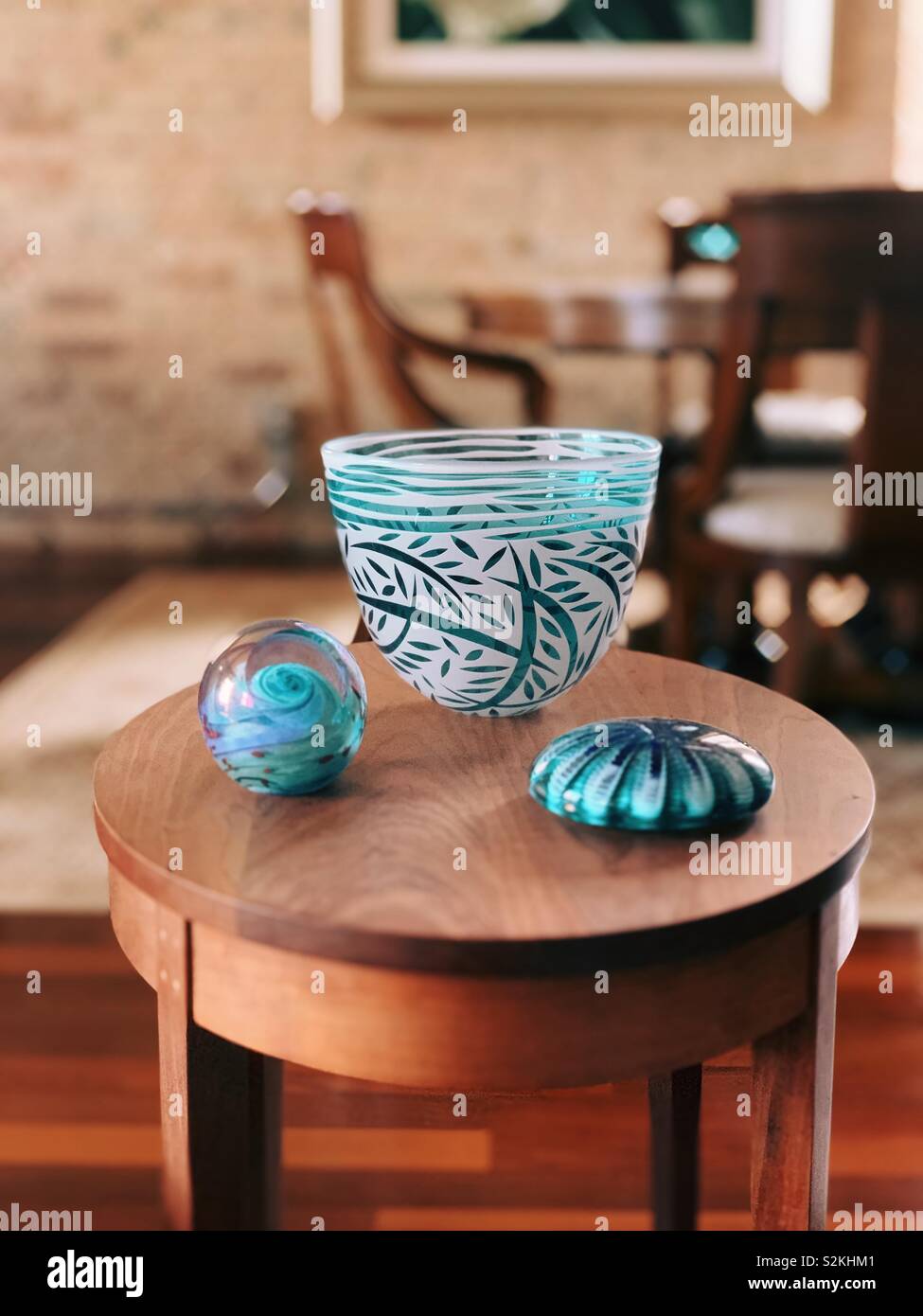 Cyan glass vase and paperweights on a wooden end table. Stock Photo