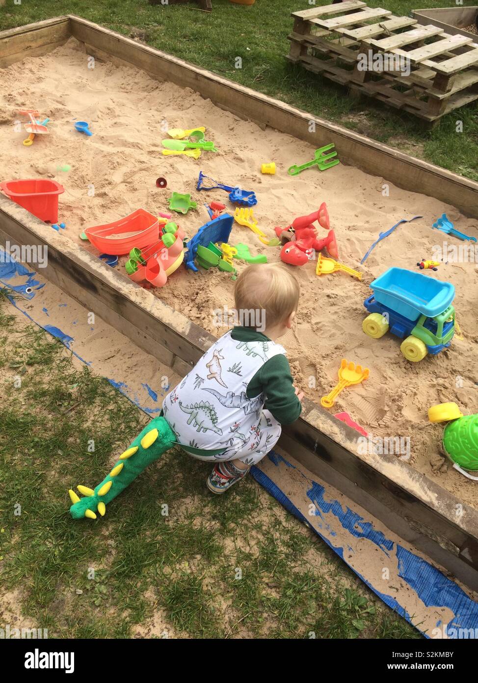 Toddler playing in sandpit wearing a Dino Tail Stock Photo