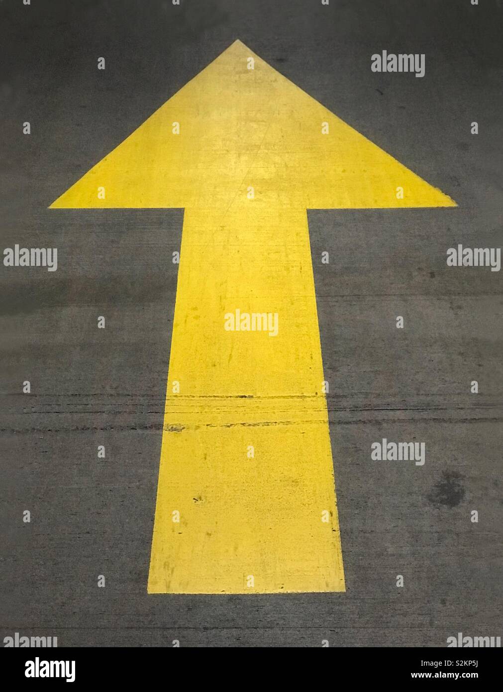 A painted, yellow, up arrow is shown on the ground surface of a parking garage. - Smartphone Captured Stock Image