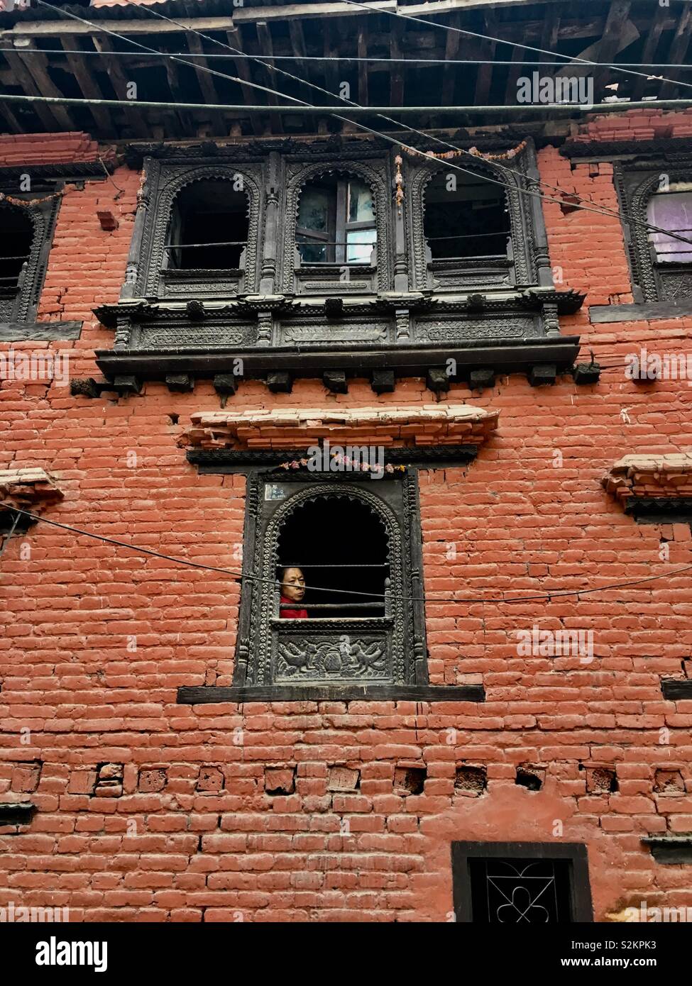 Woman looking out small window in old town Dhulikhel, Nepal. Stock Photo