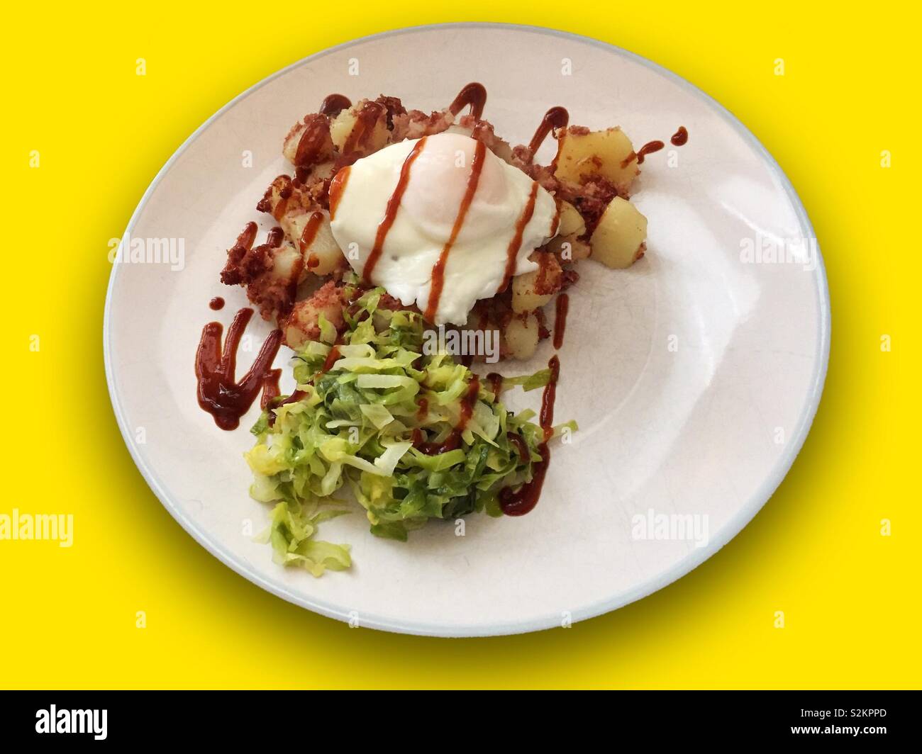 Corned beef potato hash with greens or cabbage on a colourful background.  Served with a brown sauce over the top and an egg.  Hearty food.  Filling meal cooked at home Stock Photo