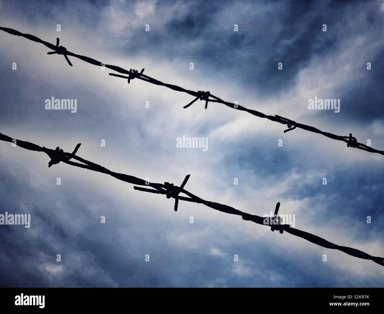 Barbed wire against dramatic blue sky Stock Photo - Alamy