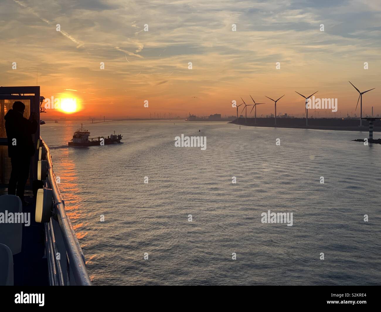 Sailing into Eurosport, Rotterdam, Netherlands at sunrise on a February morning looking towards another ship and an onshore wind farm. Stock Photo