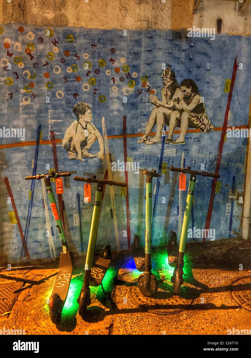 Illuminated scooters parked in front of a painted mural in Rio de Janeiro, Brazil. - Smartphone Captured Stock Image