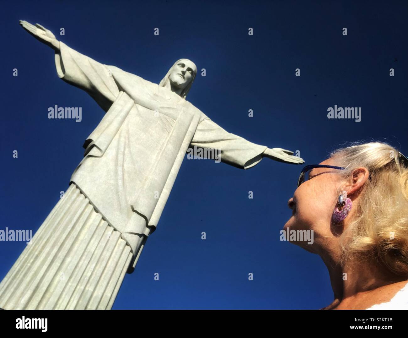 A woman looks up at the huge iconic Christ the Redeemer statue in Rio de Janeiro, Brazil. - Smartphone Captured Stock Image