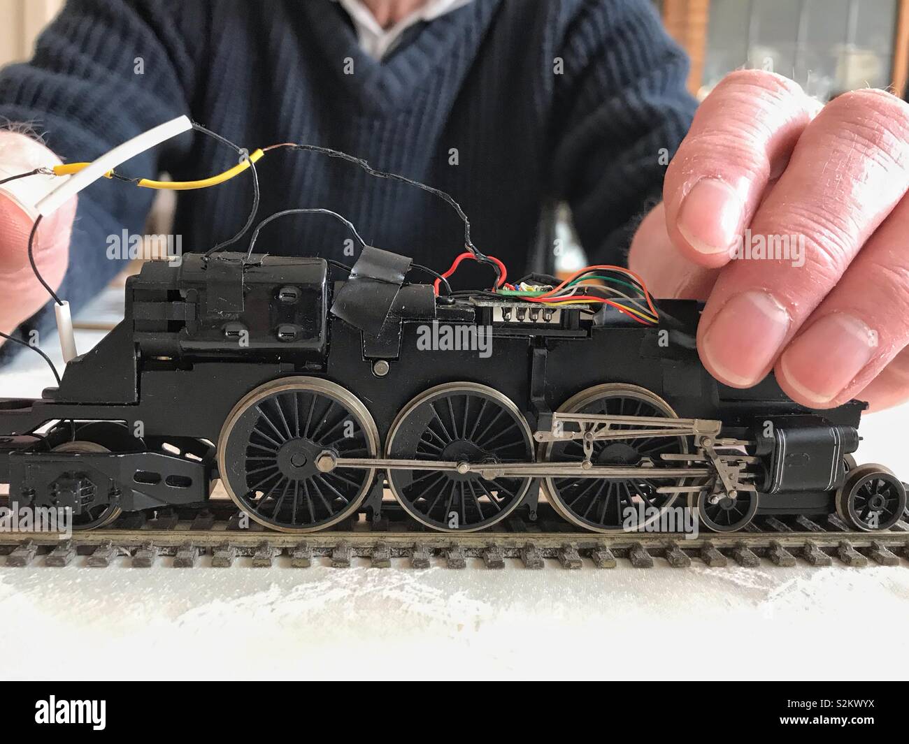 A man works on the electrics on a model locomotive. - Smartphone Captured Stock Image