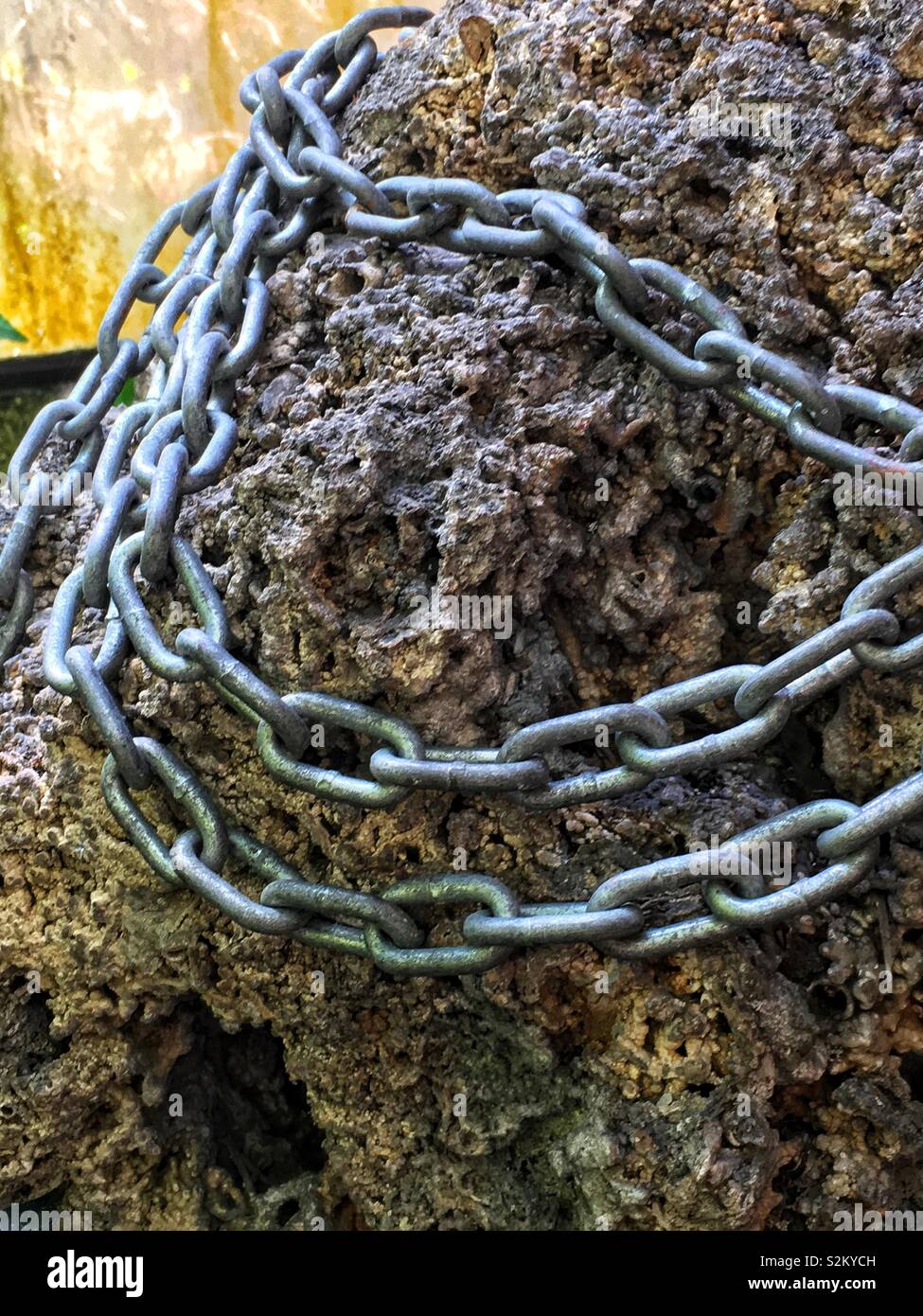 Stainless steel plated straight link chain draped over a porous limestone rock. - Smartphone Captured Stock Image