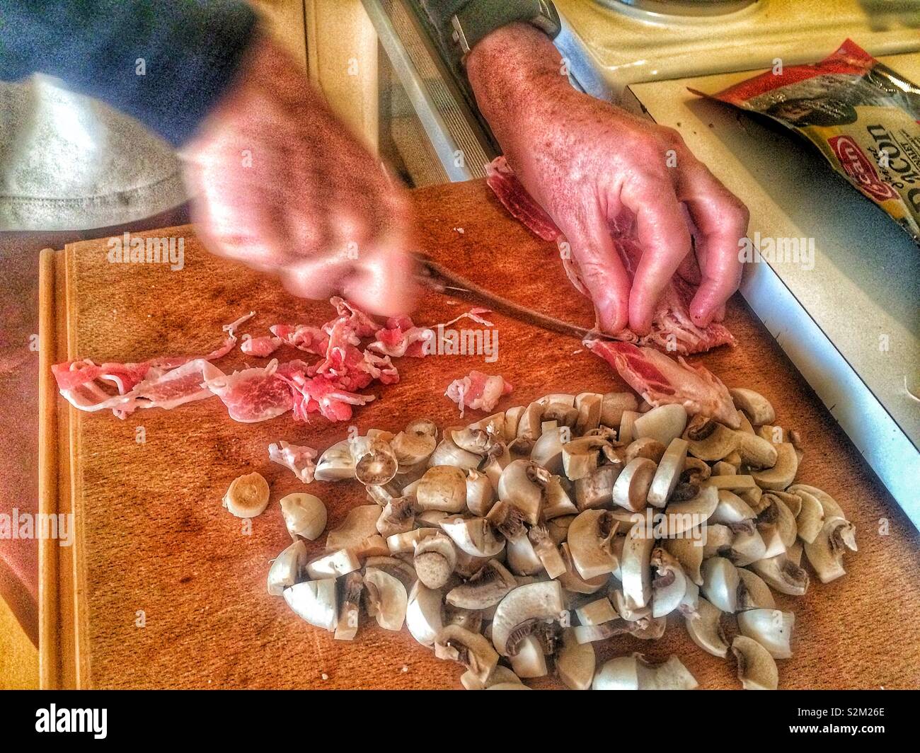 Man slicing bacon and mushrooms on pull out chopping board in a Swedish home kitchen, Sweden, Scandinavia Stock Photo