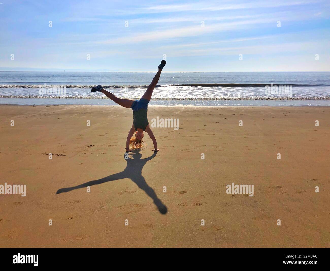 Young woman doing a cartwheel on a sandy beach. Stock Photo