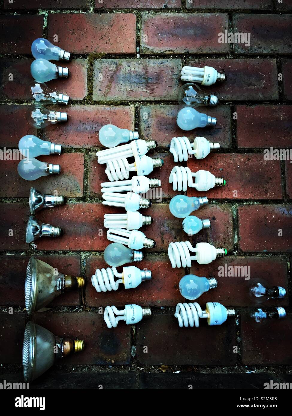 Old lightbulbs laid on a dark brownish red brick pavement. Stock Photo
