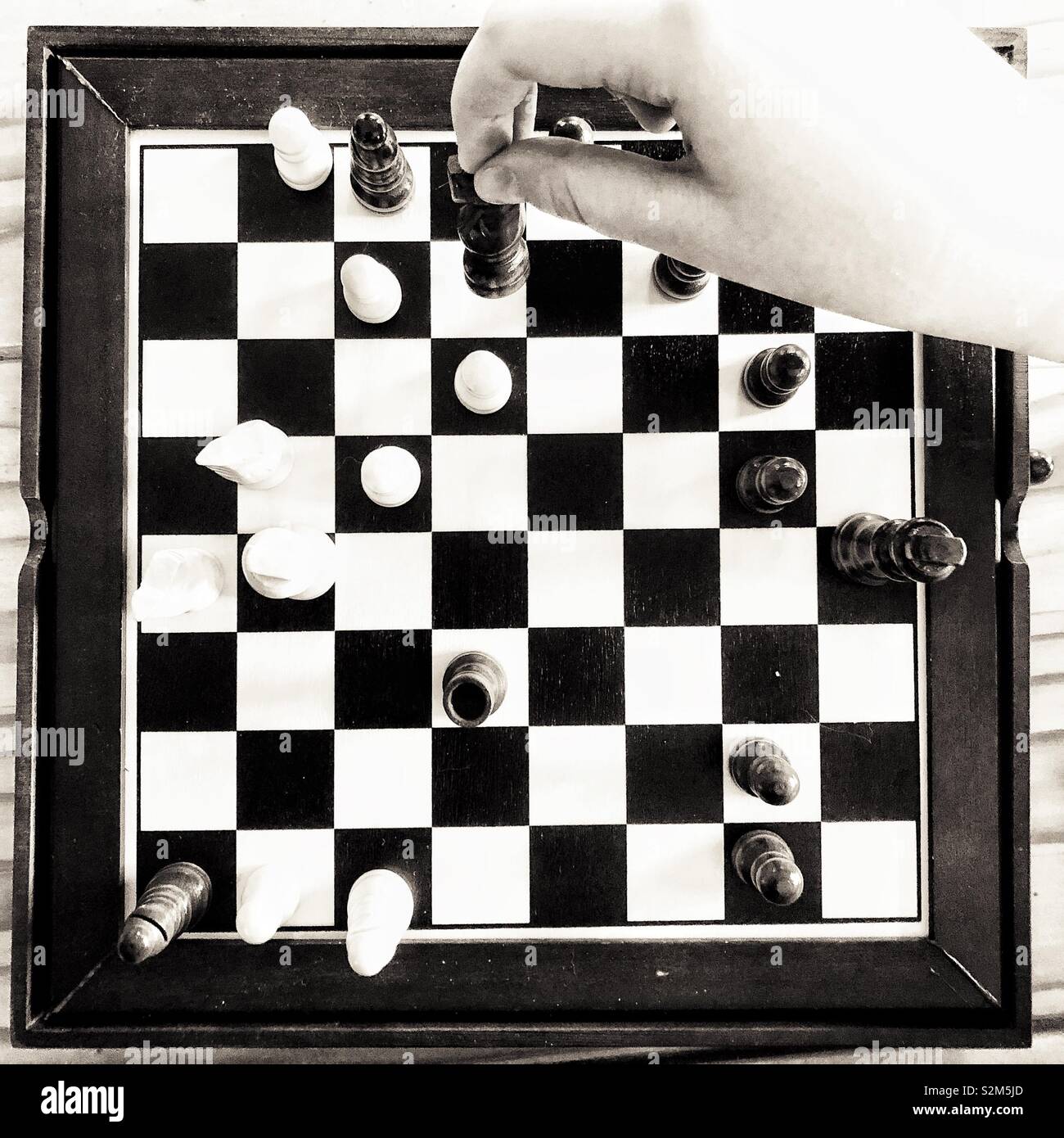 Black and white image of person’s hand playing chess on a mini board - Smartphone Captured Stock Image