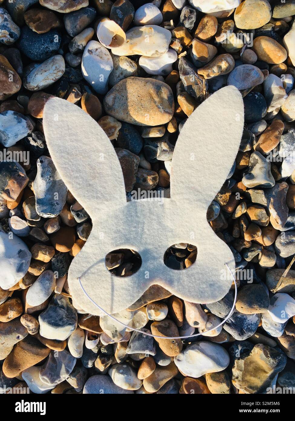Felt rabbit mask on pebbly beach - Smartphone Captured Stock Image