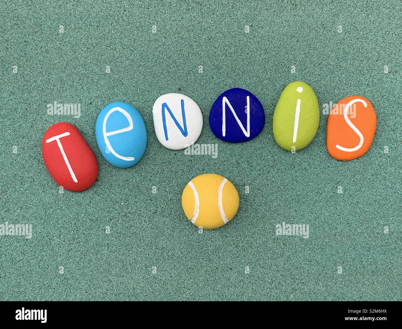 Tennis word composed with colored sea stones over green sand - Smartphone Captured Stock Image