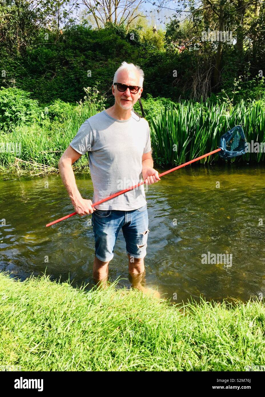 Man fishing with a kids net in a river - Smartphone Captured Stock Image