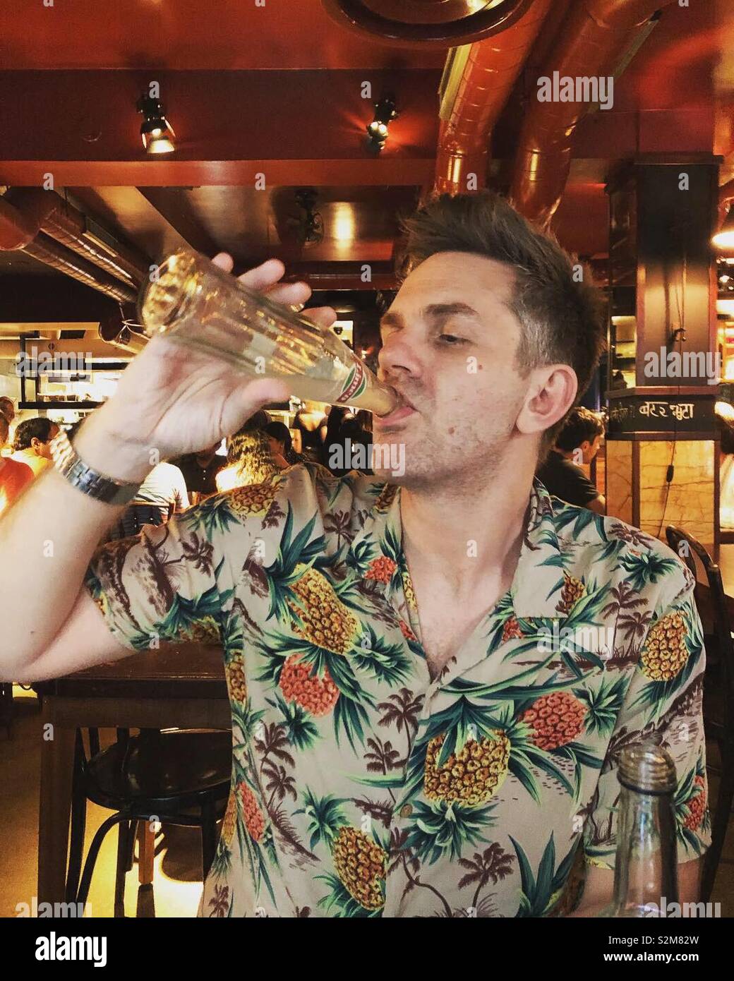 Man drinking from bottle in restaurant - Smartphone Captured Stock Image