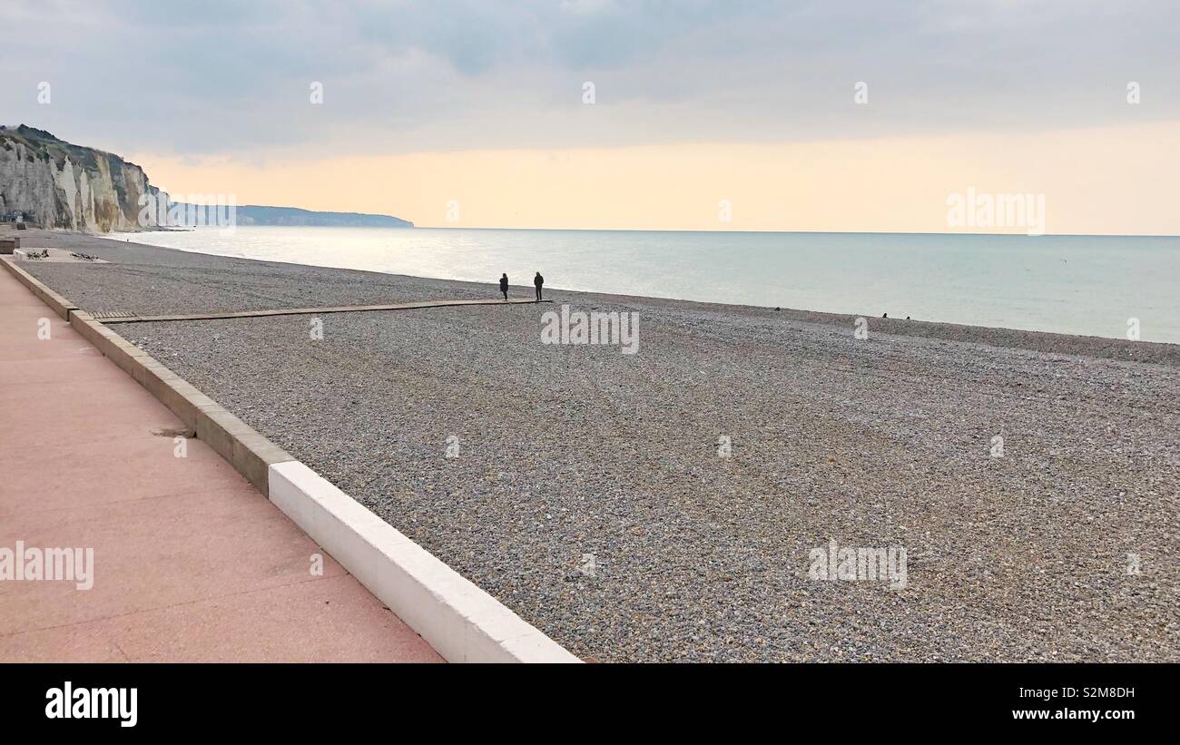 A couple at the end of a wooden walkway on The otherwise empty beach on a chilly April evening in Dieppe, France. - Smartphone Captured Stock Image