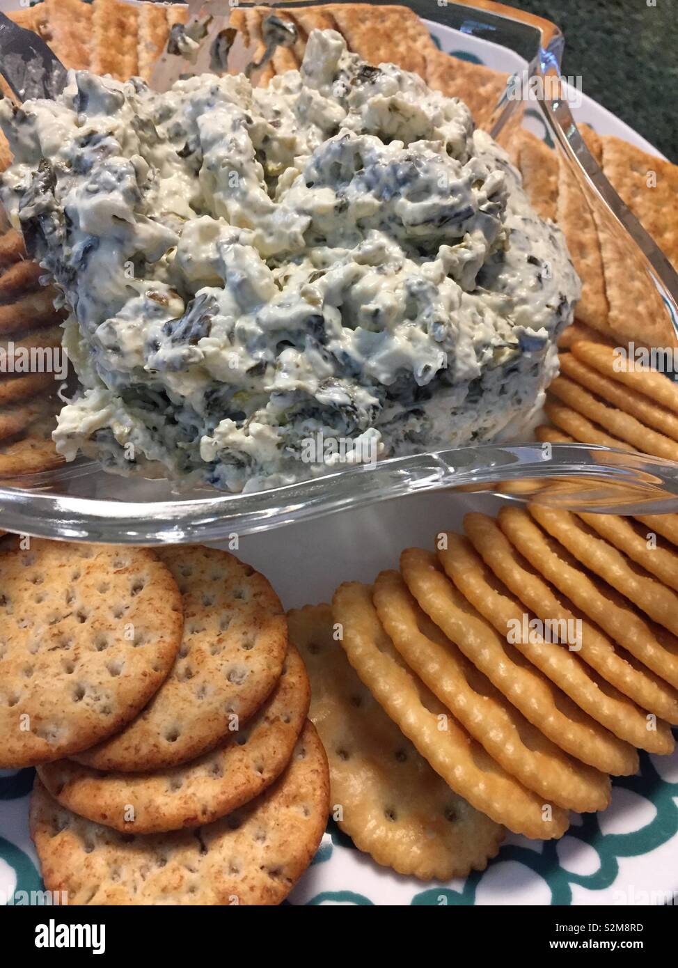 A bowl of artichoke dip on a platter of snack crackers, USA - Smartphone Captured Stock Image