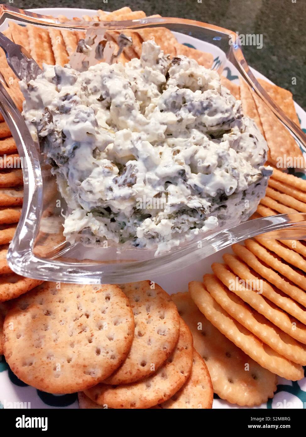 Close up of a bowl of artichoke dip on a platter with snack crackers, USA - Smartphone Captured Stock Image