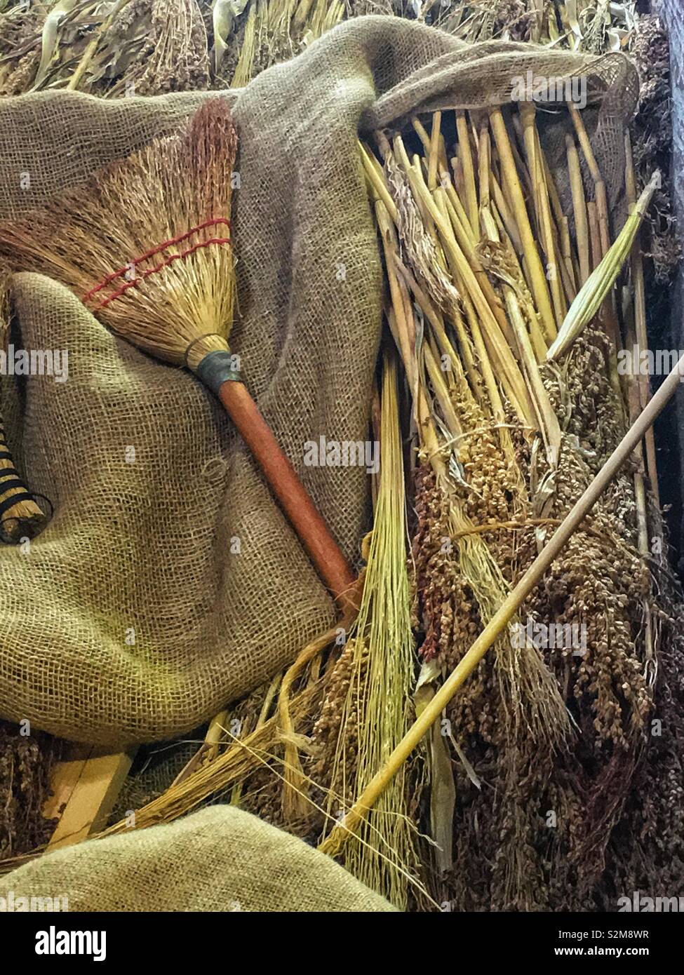 Pile of useful farm implements such as broom, shafts of wheat, and burlap blankets. Stock Photo