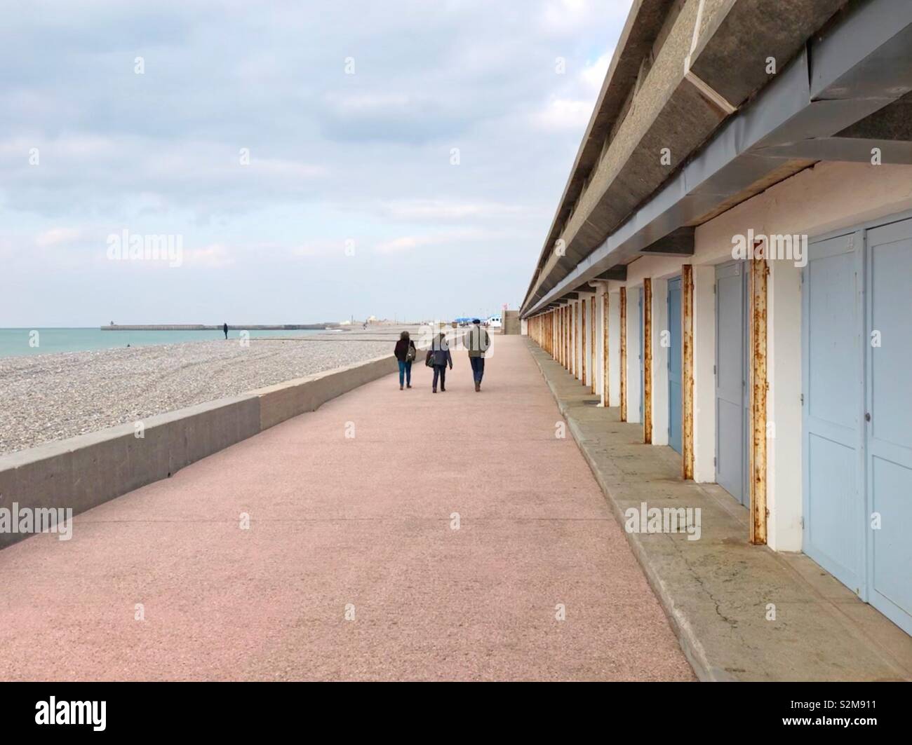 Three people walking along a row of beach cabins on the Dieppe waterfront off season. - Smartphone Captured Stock Image