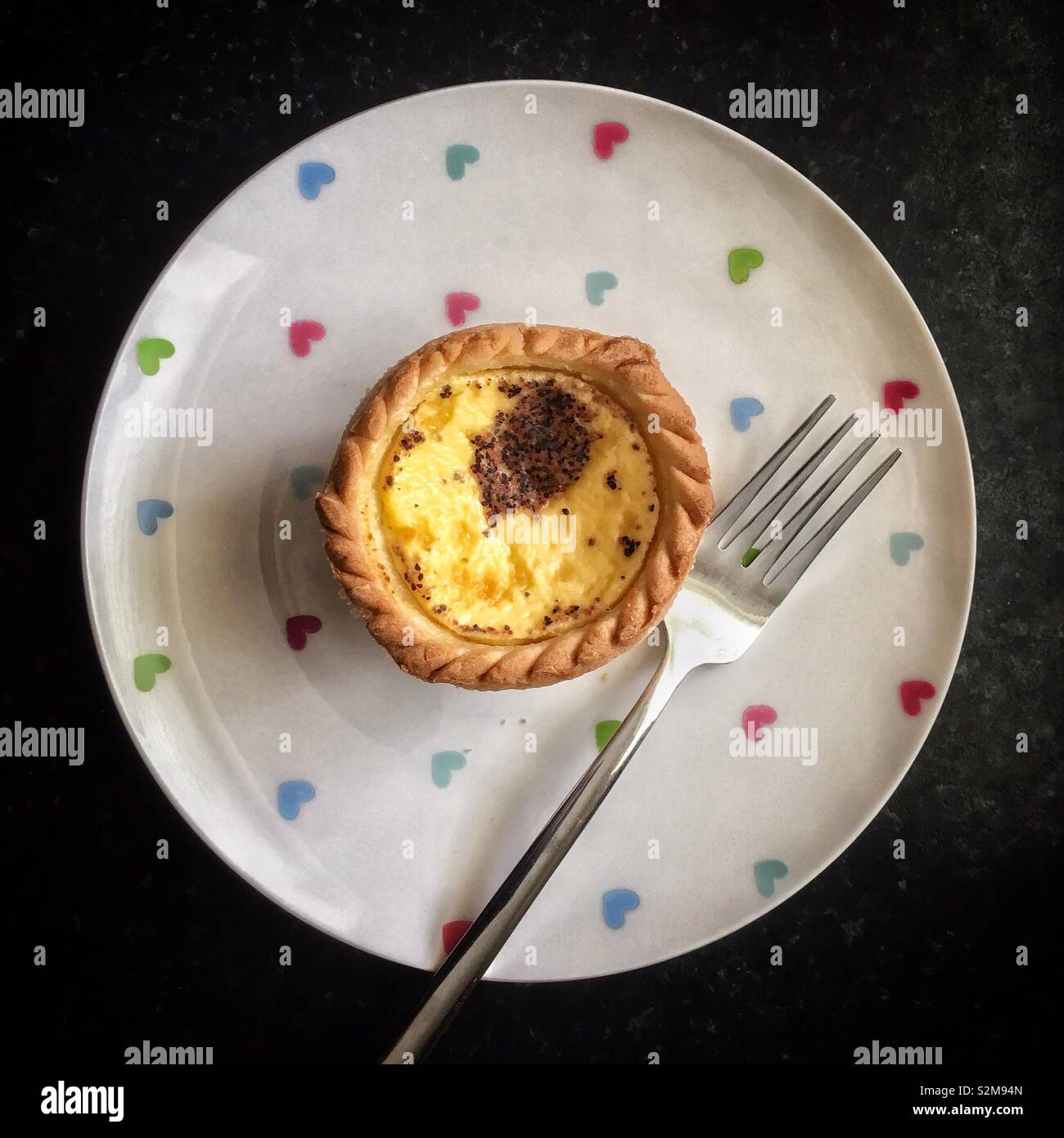 Top down view of a custard tart on a white patterned plate with a fork - Smartphone Captured Stock Image