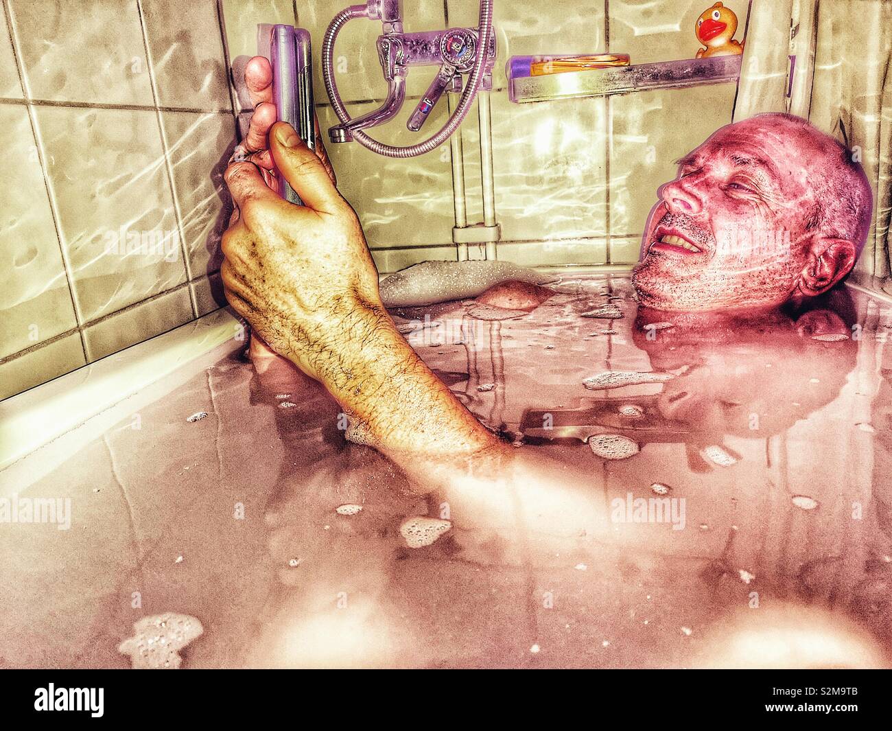 Middle aged smiling Swedish man in bath with mobile, Sweden Stock Photo