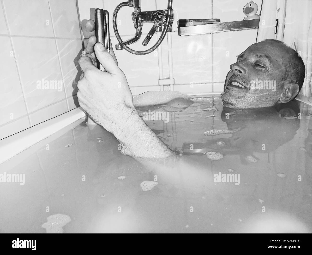Middle aged smiling Swedish man in bath with smartphone, Sweden Stock Photo
