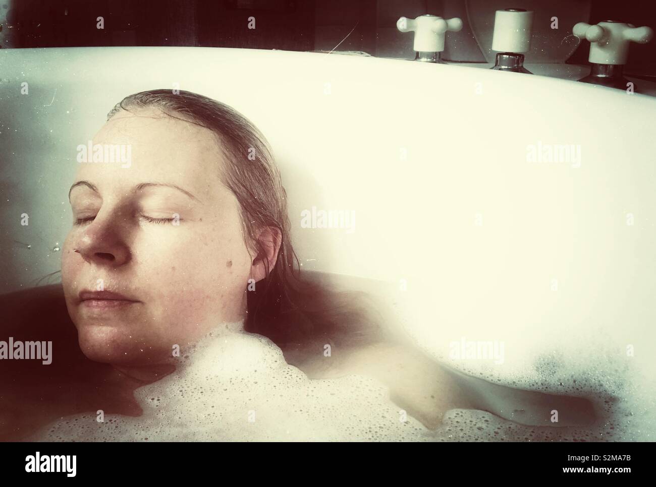 Woman relaxing in bubble bath with eyes closed - Smartphone Captured Stock Image