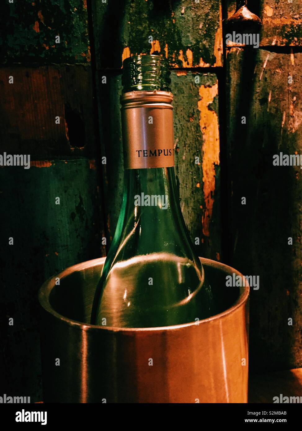White wine bottle in bucket against rustic wall. Green and orange - Smartphone Captured Stock Image