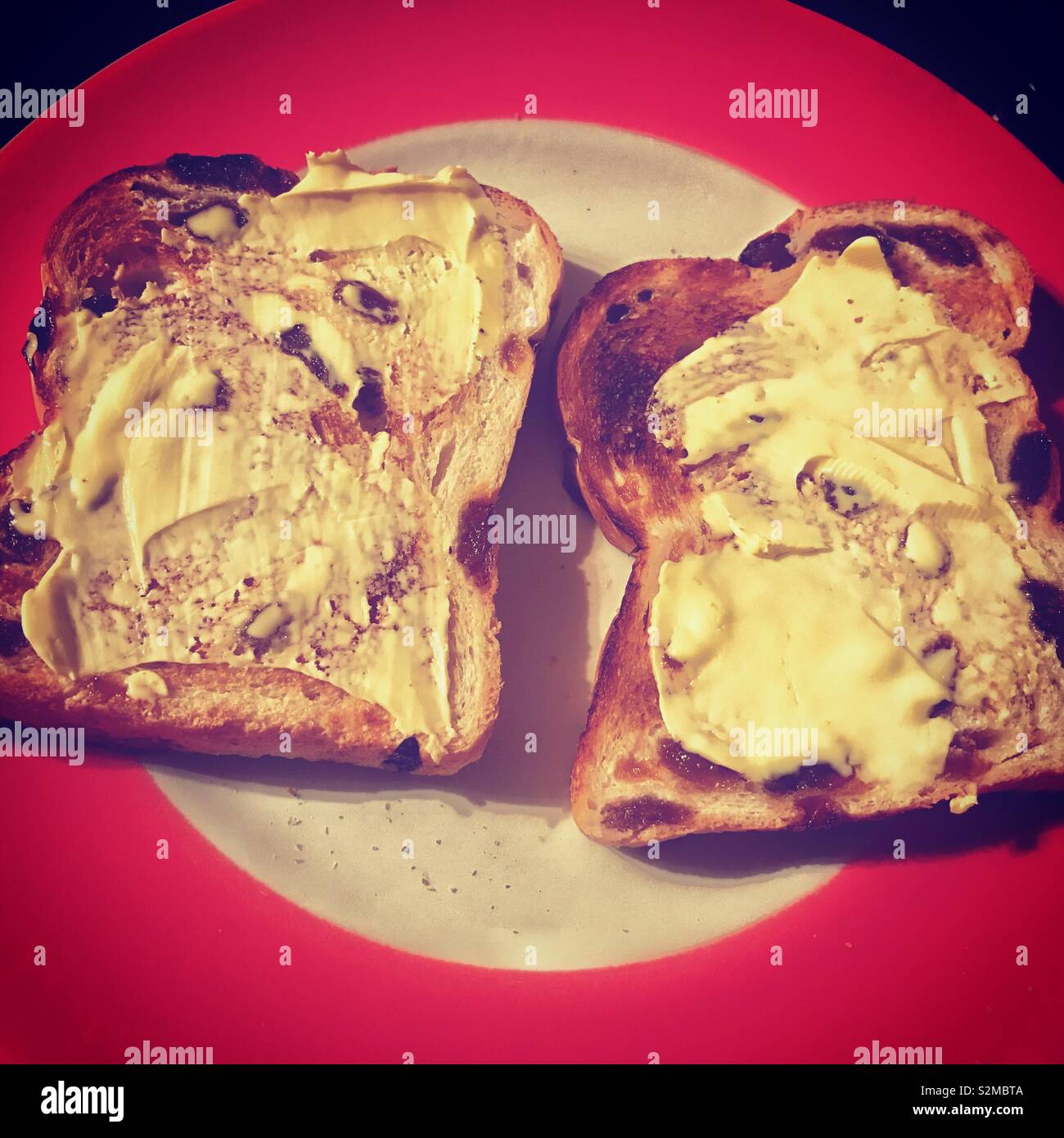 Two slices of toasted fruit loaf with butter on a red and white plate. - Smartphone Captured Stock Image