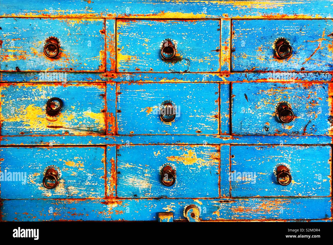 Chest of drawers with blue flaking paint and metal handles. Stock Photo