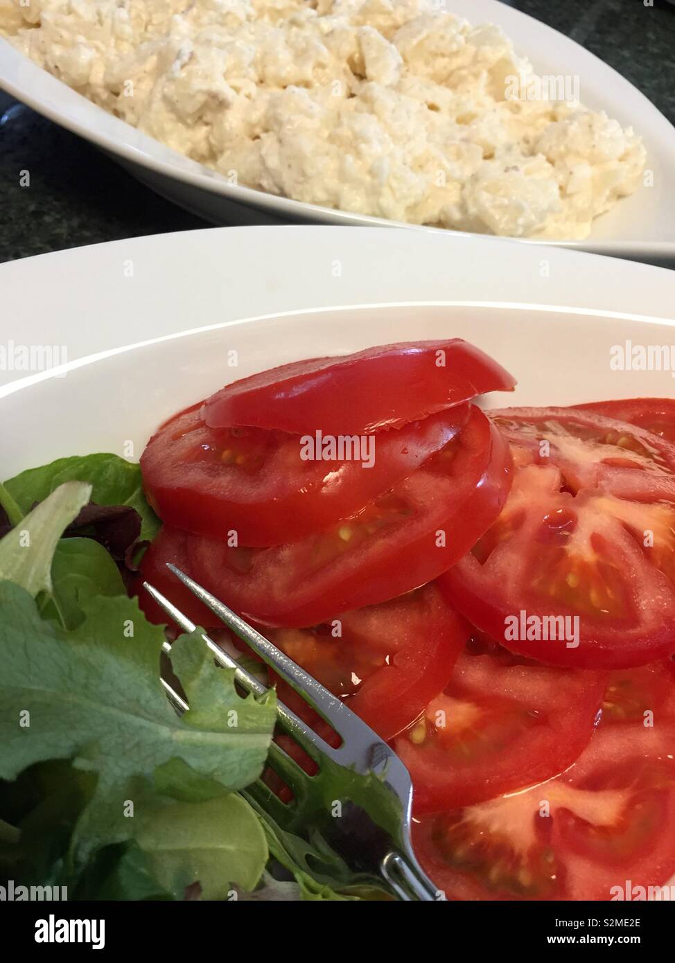A plate of sliced beef steak tomatoes and greens in front of a bowl of potato salad, USA - Smartphone Captured Stock Image