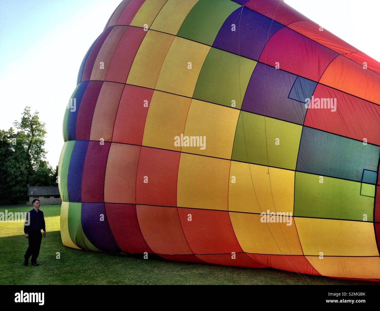 Colourful rainbow hot air balloon lying on ground beginning to fill with hot air in preparation for flight, Scotland, UK - Smartphone Captured Stock Image